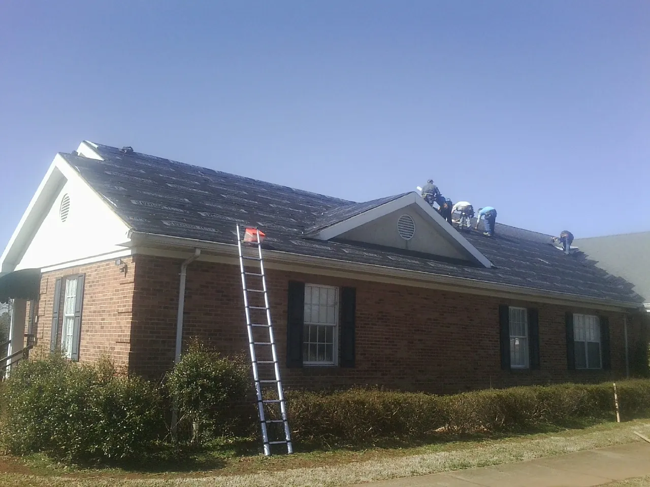 Crew tearing shingles off a brick ranch roof with a ladder set — Emergency Roof Repair work by our crew in North Hampton