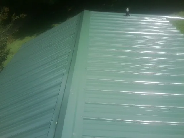 New green metal panels meeting at the ridge of a roof — Flat Roof Repair work by our crew in North Hampton