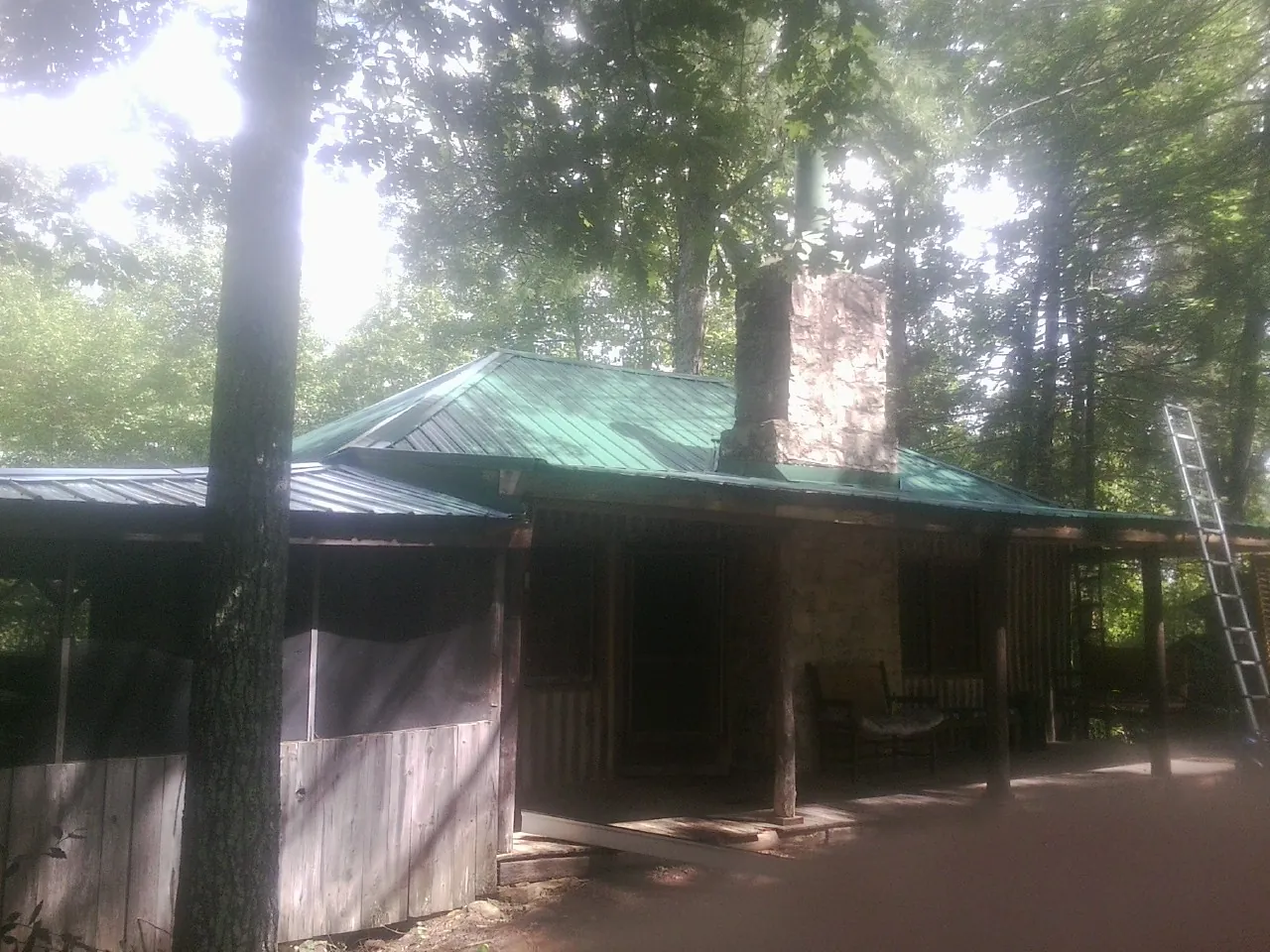 Green metal roof and stone chimney above a log cabin porch in North Hampton