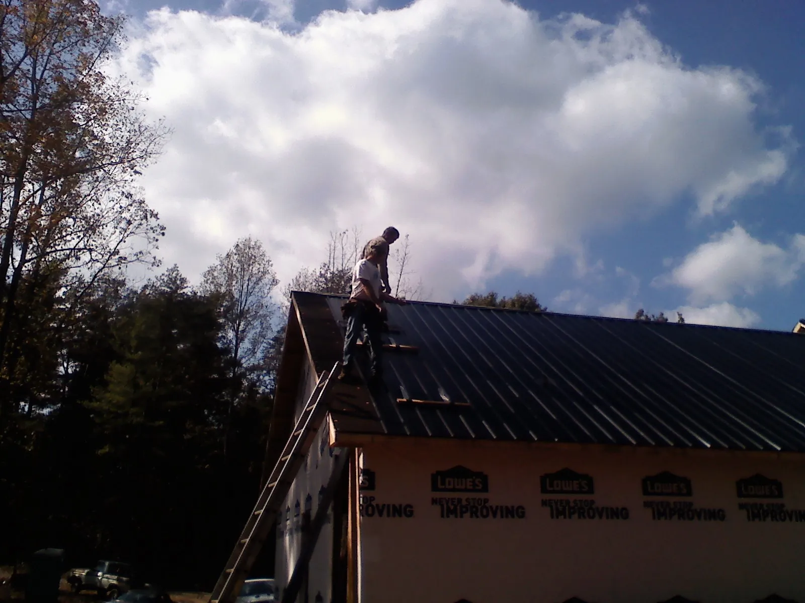 Roofer fastening dark metal panels high against a cloudy sky, from a Roof Inspection job in North Hampton