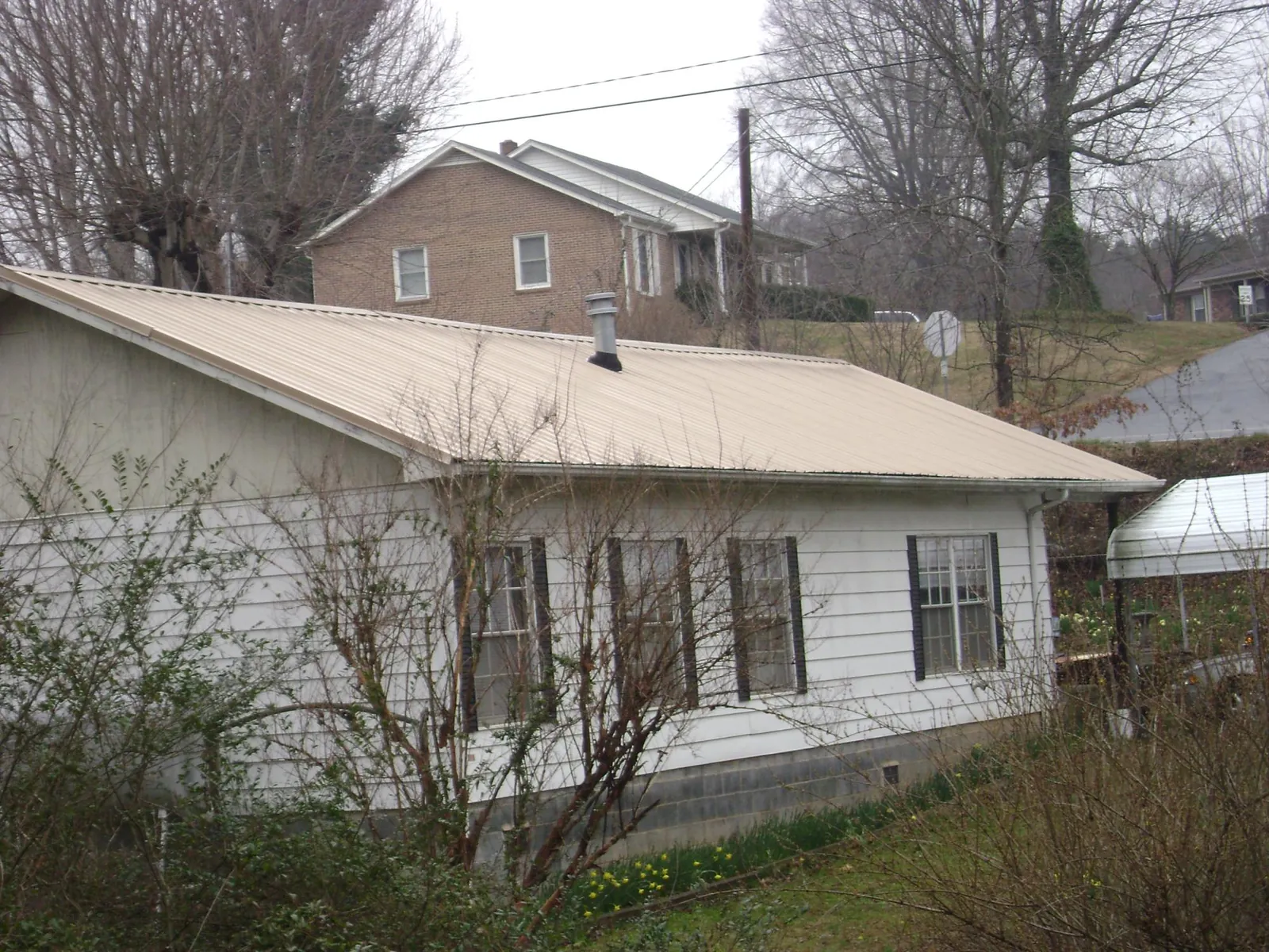Tan metal roof on a white sided house set into a hillside — Commercial Roofing by Roofing Brothers in North Hampton