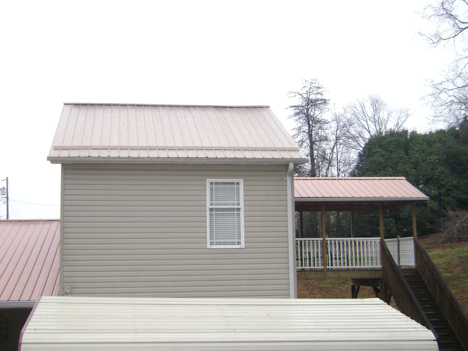 Tan metal roofs on a two story addition and attached porch, from a Roof Replacement job in North Hampton